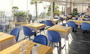 Restaurant med borde dækket med gule duge og blå stole. (AI-genereret tekst)