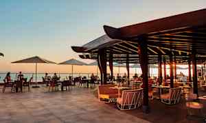 Åben restaurantterrasse med udsigt over havet ved solnedgang. (AI-genereret tekst)