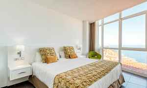 Et hotelværelse med en redt seng, store vinduer og udsigt over havet. (AI-genereret tekst)