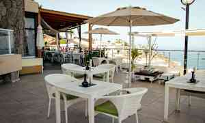 En terrasse med borde og stole samt udsigt over havet. (AI-genereret tekst)