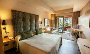 Et hotelværelse med en stor seng, sofa og skrivebord. Der er også en balkon med udsigt. (AI-genereret tekst)