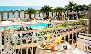 Udsigt fra en balkon med morgenmadsservering mod poolområde og havet. (AI-genereret tekst)