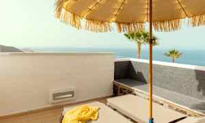 En liggestol på en terrasse med udsigt over havet, parasol og palmer. (AI-genereret tekst)