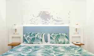 Seng med grønt og hvidt mønstret tæppe og puder, med blå sengegavl og hvide vægge. (AI-genereret tekst)