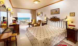 Et hotelværelse med en dobbeltseng, siddeområde og en balkon med udsigt mod havet. (AI-genereret tekst)