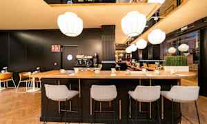 Interiør af en moderne café- eller bardel med højbord og stole, kaffemaskine og belysning. (AI-genereret tekst)