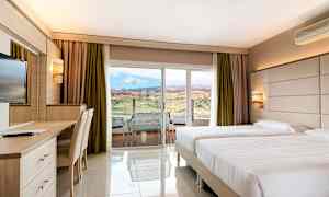 Hotelværelse med to enkeltsenge, skrivebord og udsigt til landskab gennem en glasdør. (AI-genereret tekst)