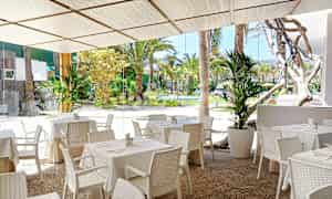 Udendørs restaurant med hvide borde og stole samt udsigt til en frodig have. (AI-genereret tekst)