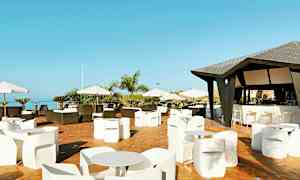 En terrasse med borde og stole samt en bar med tag. Der er parasoller og udsigt over himlen og træer. (AI-genereret tekst)