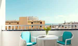 En altan med to stole, et bord og udsigt over bygninger og havet. (AI-genereret tekst)