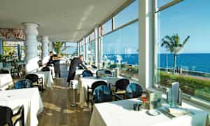 Restaurant med dækkede borde tæt på vinduer med havudsigt. (AI-genereret tekst)