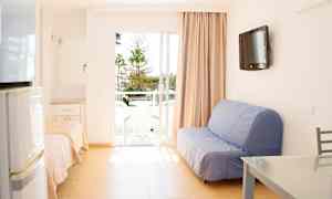 Et lyst rum med sofa, bord og en balkon med udsigt over træer. (AI-genereret tekst)