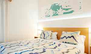 Seng med to puder og et tæppe i et lyst rum. (AI-genereret tekst)