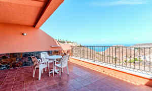 Terrasse med bord, stole og rækværk, samt havudsigt. (AI-genereret tekst)