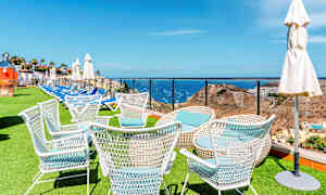 Hvide havemøbler på en græsplæne med havet og landskabet i baggrunden. (AI-genereret tekst)