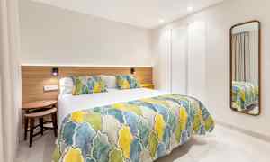 Et moderne hotelværelse med en seng med farverigt sengetæppe og puder samt et spejl på væggen. (AI-genereret tekst)