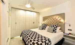 Et moderne soveværelse med en dobbeltseng, knap hovedgærde og mønstret sengetøj. (AI-genereret tekst)