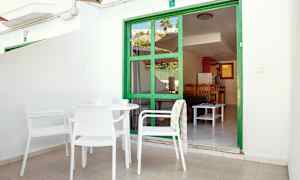 Terrasse med hvide møbler foran en grøn dørramme, der fører ind til en lejlighed. (AI-genereret tekst)