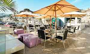 Udendørs terrasse med borde, stole og parasoller, omgivet af bjerglandskab. (AI-genereret tekst)