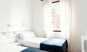 Et hotelværelse med to enkeltsenge med hvide lagner og blå tæpper. (AI-genereret tekst)