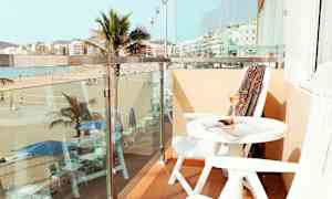 En balkon med udsigt over en strand og palmer, med bord og stole. (AI-genereret tekst)