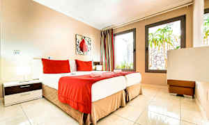 Et hotelværelse med en seng redt med rødt og hvidt sengetøj samt store vinduer. (AI-genereret tekst)