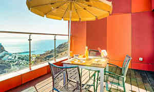 En terrasse med bord, stole og parasol med udsigt over havet. (AI-genereret tekst)