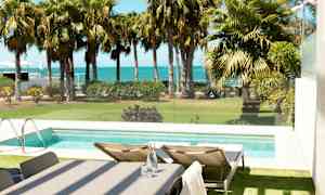 Udsigt over en pool med liggestole ved siden af, have med palmer og havet i baggrunden. (AI-genereret tekst)