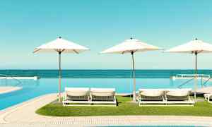 Udsigt over liggestole med parasoller ved en infinitypool, havet i baggrunden. (AI-genereret tekst)