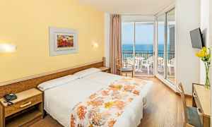 Hotelværelse med to senge, gult interiør og en balkon med udsigt over havet. (AI-genereret tekst)