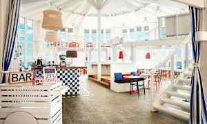 En indendørs bar med hvide og røde møbler samt store vinduer. (AI-genereret tekst)