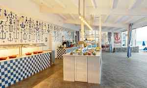 Billede af en buffetrestaurant med maritimt tema, med opdækkede borde og dekorationer. (AI-genereret tekst)