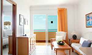 En stue med sofa, bord og udsigt til havet gennem en glasdør. (AI-genereret tekst)