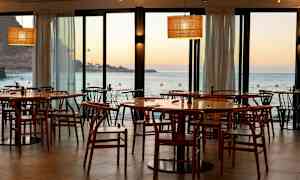 Restaurant med træstole og borde med udsigt over havet og solnedgang. (AI-genereret tekst)