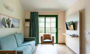 En stue med en blå sofa, en fletstol og et TV monteret på væggen. (AI-genereret tekst)