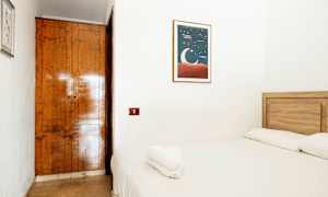 Et lille værelse med en træbed og hvidt sengetøj. På væggen hænger et billede med en måneillustration. (AI-genereret tekst)