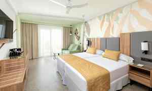 Et hotelværelse med to senge, en sofa og et dekorativt vægdesign. (AI-genereret tekst)