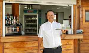 En person holder en bakke med to glas foran en serveringsdisk af træ. (AI-genereret tekst)