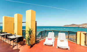 En terrasse med udsigt over havet, udstyret med liggestole, borde og stole. (AI-genereret tekst)