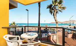 Udsigt fra en altan med bord og stole mod havet og stranden. (AI-genereret tekst)