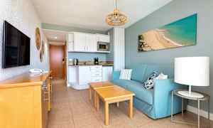 Lejlighedsværelse med blå sofa, træmøbler og køkkenområde. (AI-genereret tekst)