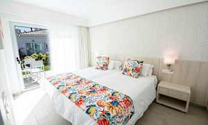 Et hotelværelse med to enkeltsenge, farverige pudebetræk og en dør til en terrasse. (AI-genereret tekst)