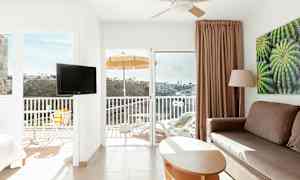 Interiør af et lyst hotelværelse med balkon, udsigt over en dal. (AI-genereret tekst)