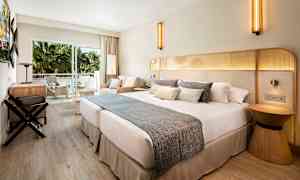 Et hotelværelse med en stor dobbeltseng, siddeområde og altan med udsigt til grønne palmer. (AI-genereret tekst)