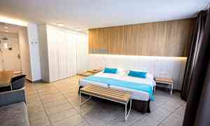 Et moderne hotelværelse med en dobbeltseng, en træbænk for enden og et skrivebord i hjørnet. (AI-genereret tekst)