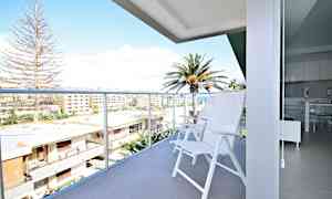 En altan med hvide stole og udsigt over bygninger og palmer. (AI-genereret tekst)