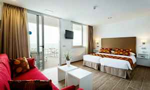 Et moderne hotelværelse med to enkeltsenge, røde sofaer og en altan med havudsigt. (AI-genereret tekst)