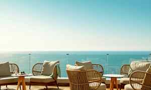 Loungeområde med siddepladser, et glasrækværk og udsigt over havet. (AI-genereret tekst)