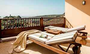 To liggestole med stribede hynder står på en terrasse med udsigt over frodige bakker. (AI-genereret tekst)