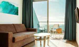 En stue med sofa og bord, med en altan og udsigt over havet. (AI-genereret tekst)